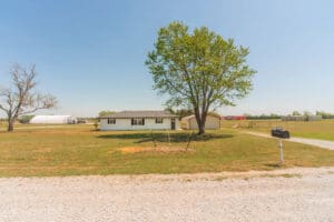Rural house with tree and gravel road.
